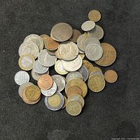 Pile of various coins and tokens on a dark surface showing different colors, sizes, and designs.