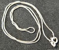 Close-up photo of the sterling silver chain coiled on a black background showing box-link style and spring ring clasp, stamped 925.
