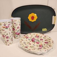 Four floral melamine cups, four matching floral melamine plates stacked, and a vintage painted green tray with a yellow flower decoration