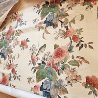 Roll of vintage fabric spread out showing floral and leaf patterns with birds.