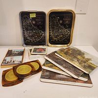 Photo showing two small metal trays with Barbados map design, three vintage coaster sets, and a set of vintage art table mats stacked.