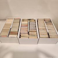 Three white storage boxes full of assorted trading cards primarily from 1990s sports and Marvel categories.