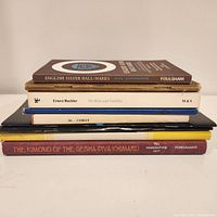 Stack of seven books showing titles on spines: English Silver Hall-Marks, Ernest Buckler, Corot, The Kimono of the Geisha Diva Ichimaru and two others.