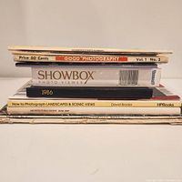 Stacked vintage photography books, magazines and an almanac. Titles include Good Photography, Household Hints Almanac, Showbox Photo Viewer, 1986 Photography by David Brooks, and How to Photograph Landscapes & Scenic Views.
