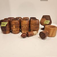 Photo capturing 12 wood tiki-style cups, one finely turned wooden stemmed cup, a wooden nut cracker, and a wine stopper with cork on a white background.