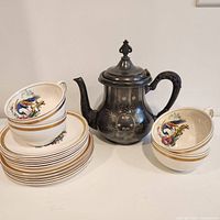 Full view of 4 cups stacked on 6 saucers and 5 side plates along with silverplate kettle
