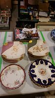 Photo showing the sets of antique luncheon and dessert plates including Limoges plates in pink and green, Coalport blue plates, and Claire Bavaria plates.