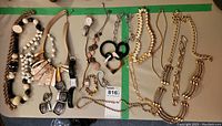 Wide view of entire lot showing multiple necklaces, two wristwatches, bracelets, and earrings laid out on surface.