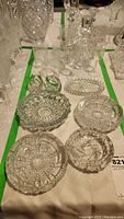 Top view of four crystal ashtrays and crystal whiskey decanter with stopper arranged on a white tablecloth