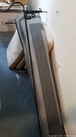 Four beige chair cushions and long gray outdoor patio mat leaning against a wall in a basement.