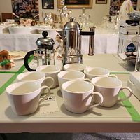 Photo showing eight white mugs, stainless steel French press, and stainless steel Kontessa espresso maker with wooden handle
