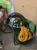Coiled dark and light green garden hoses with yellow extension cord on carpet