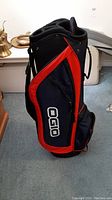 Side view of navy blue and red OGIO golf bag showing the logo and side zip pocket