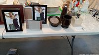 Photo showing two Lampe Bergers, four tumblers, five picture frames and bathroom accessories on table
