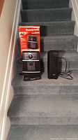 Photo of two portable heaters on carpeted stairs, includes Honeywell heater in box and Seville Classics heater.
