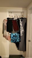 Photo showing a collection of women's clothing hanging on a door rack including various dresses, pants, and a shawl.