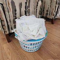 Plastic laundry bin filled with various white and lace table linens including napkins and tablecloths shown on top