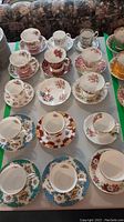 Full set of tea cups and saucers on table with floral patterns in various colors.
