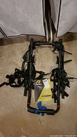 Full front view of the black framed Raleigh trunk mount bike rack resting on floor with owner manual laid on top.