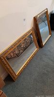 Two wall hanging mirrors displayed side by side against a wall on carpeted floor.