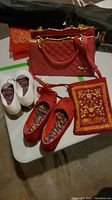 Photo showing two pairs of women's shoes (white and red), red quilted handbag, red embroidered purse, and small red bag arranged on a white table