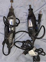 Two Dremel rotary tools, power cords visible, tools laid on a surface, showing overall lot contents