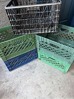 Photo showing one black crate stacked on top of four crates (two green, one blue, one green partially visible)
