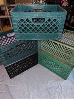 View of five plastic crates stacked and arranged on a cloth backdrop showing various colors and lattice pattern sides.