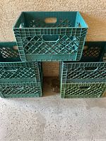 Five green plastic stackable crates arranged with one on top, four on bottom against a textured wall on concrete floor.