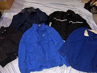 Five jackets laid flat on a bed, two blue and three black.