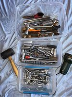 Three clear plastic containers filled with socket wrench attachments, ratchet handles, and other hand tools including a rubber mallet.