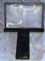 Front view of the large rectangular magnifying glass resting on a surface showing the lens and black plastic stand folded out.