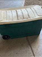 Side view of large green Rubbermaid storage container with beige lid and two wheels.