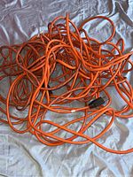 Coiled long orange electrical extension cord with a black plug on one end, lying on a blue surface.