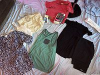 Overview of various clothing items including men's tank tops, polo shirt, women's blouses, and accessories on a bed.