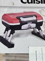 Side view of the red and black portable gas grill with foldable legs and Cuisinart branding on the lid and handle.