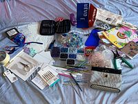 Photo showing the assorted beads in plastic containers, crochet pins and tools like wire cutters, scissors, pencils, and other art supplies spread on fabric.