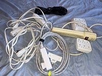 Four extension cords, three power strips, and two adapters seen together on a blue fabric surface.