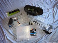 Photo showing assorted plastic tool organizers of various sizes, a black cloth toolbox with tools inside, and a charger device