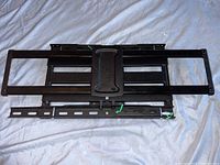 Top view of the black metal wall mount laid flat on a white fabric background showing adjustable arms and central mounting plate.