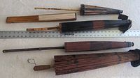 Four Asian umbrellas laid out horizontally with a ruler for scale, showing wooden handles and ribs with signs of wear and discoloration.