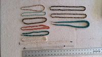 Overview of 11 assorted bead, stone, and shell necklaces laid on light fabric, showing size range and colors including orange, brown, turquoise, white, black beads.
