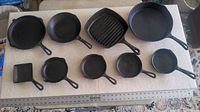Photo showing all eight assorted cast iron pans including round, square, grill, and small rectangular pans lined up with ruler for size reference.