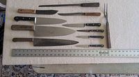 Full laydown of assorted knives and carving fork next to a ruler for size reference.