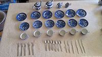 Photo shows the entire Blue Willow children's tea service with all ceramic pieces including 2 teapots, creamer, sugar bowl, 6 plates, 6 saucers, and 6 cups. Also laid out are 6 spoons, 5 forks, 2 butter utensils and 2 regular utensils.