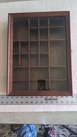 Closed wooden shadow box with glass front showing grid compartments behind glass.