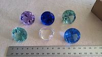 All six glass paperweights arranged with ruler for scale. Five diamond-shaped colored glass pieces with one clear heart-shaped.
