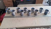Ten white ceramic mugs arranged in a single row on table with ruler at front.