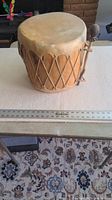 Rawhide and wood drum front and top view showing drumhead and lacing pattern on wooden body alongside a ruler for scale.