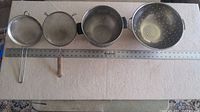 Top view of two sieves and two colanders arranged on a surface with measuring ruler showing sizes.